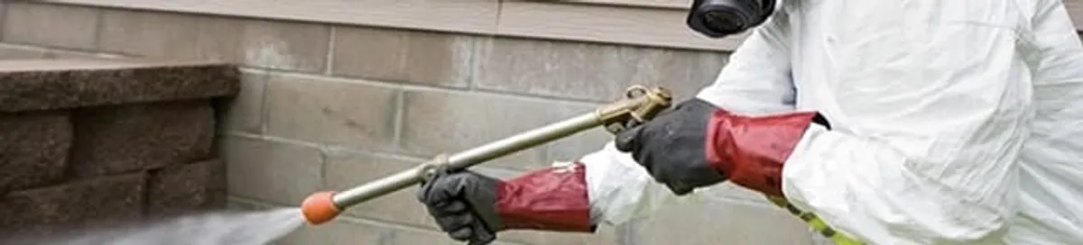 Pest control technician applying exterior insect treatment along a home foundation in Des Moines, IA