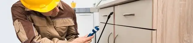 Roach exterminator applying treatment under kitchen cabinets in Des Moines, IA