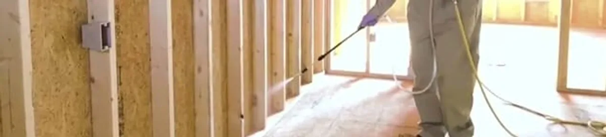 Termite treatment technician applying spray along framing and unfinished walls in Des Moines, IA